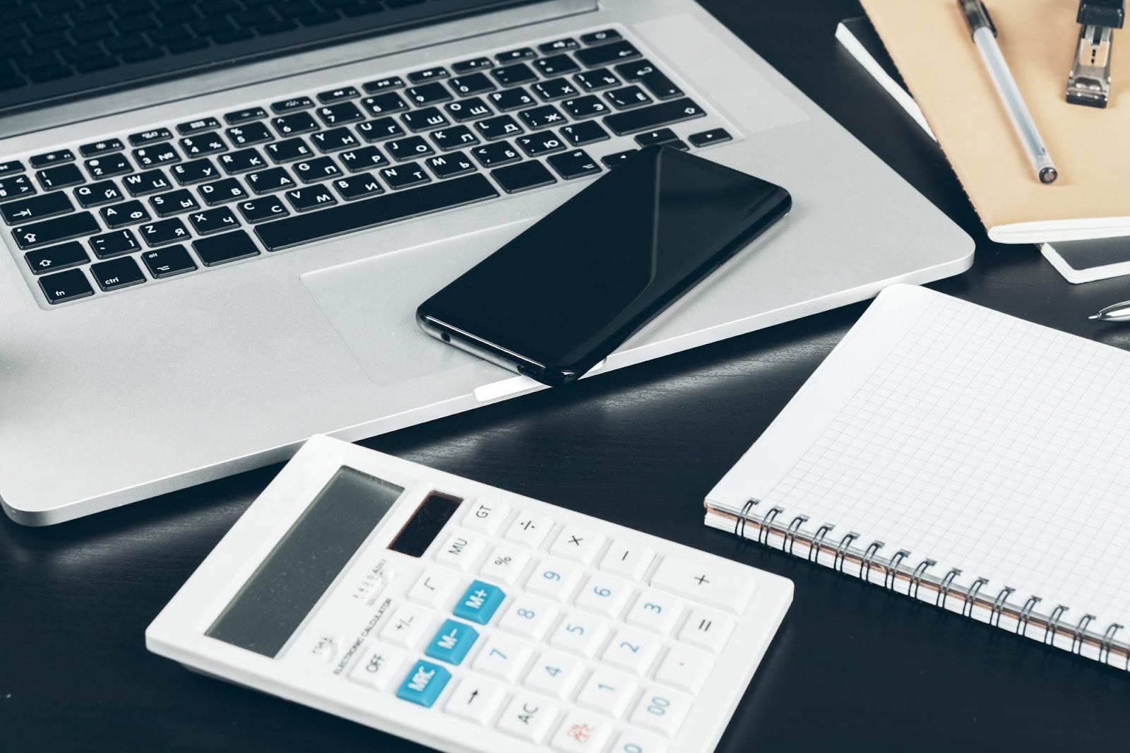 Image displaying a notepad, calculator, phone, and laptop